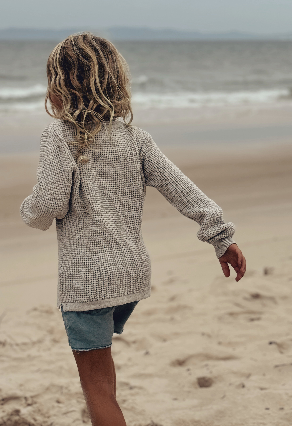 boy walking on sand at the beach showcasing the back of waffle speckle pull over