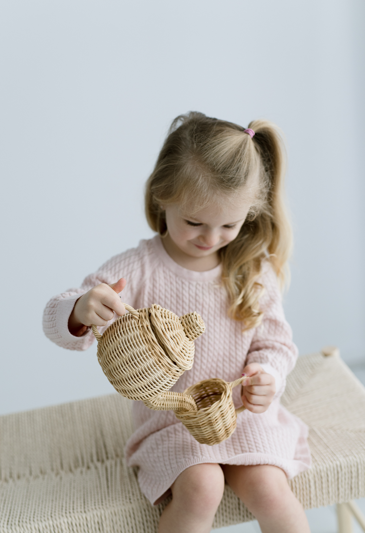 Young girl in a pink dress playing with woven toys on a light background