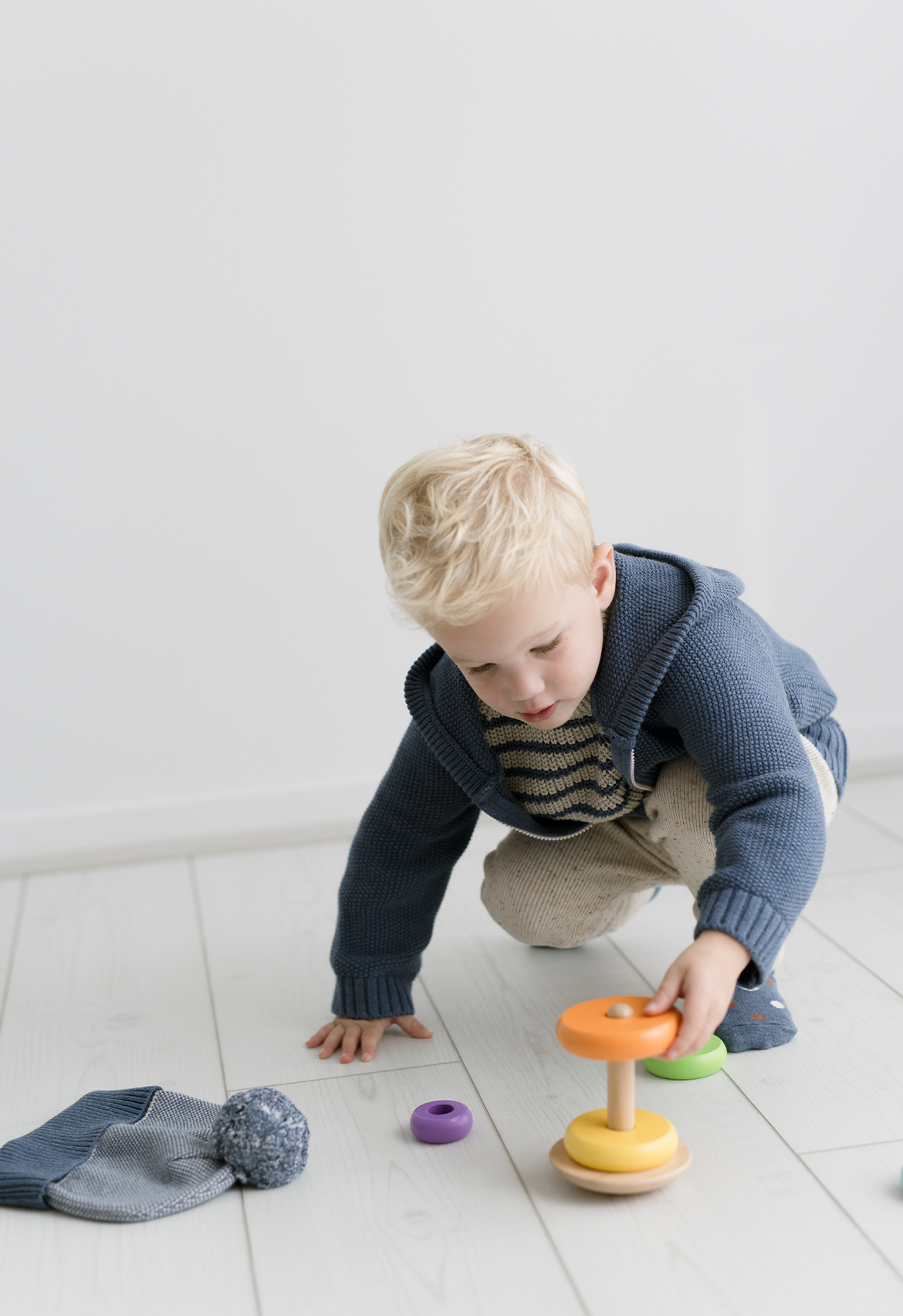 Child playing with colorful toys on a light wooden floor in knit hooded jacket