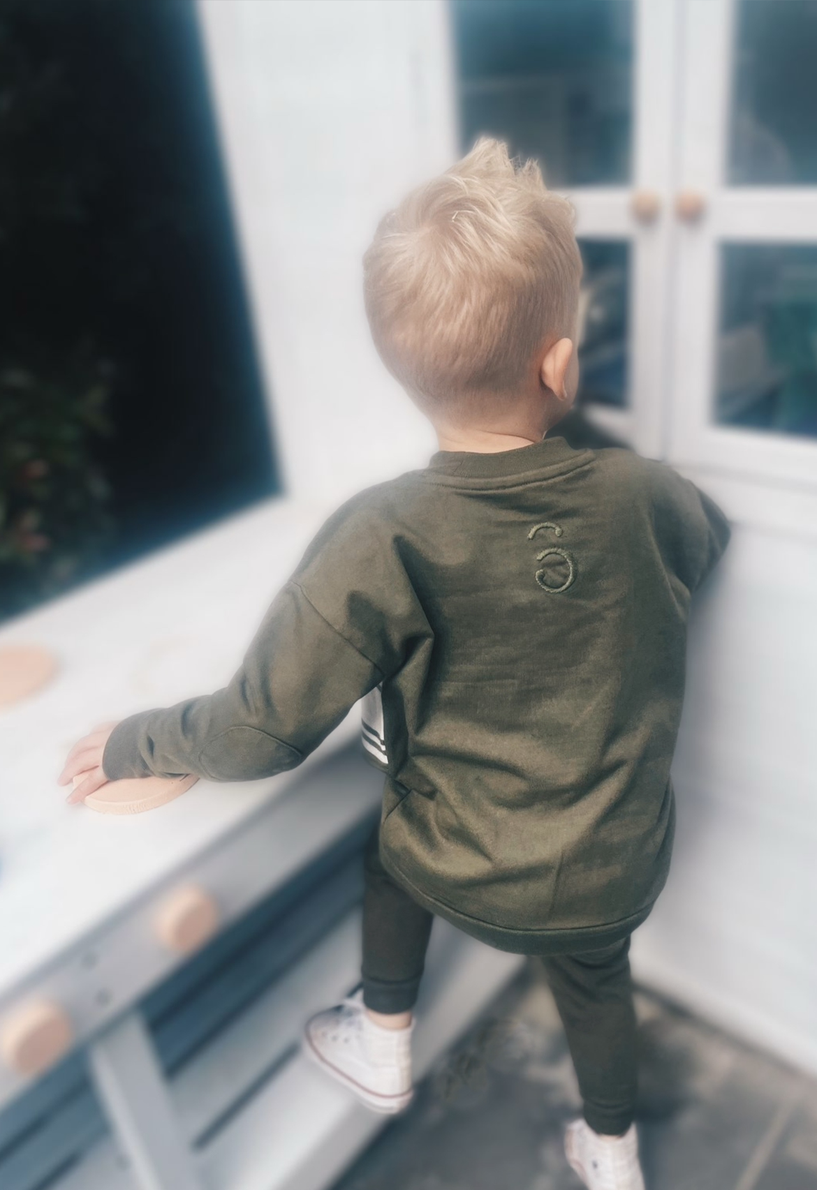Child wearing an olive jumper with a logo