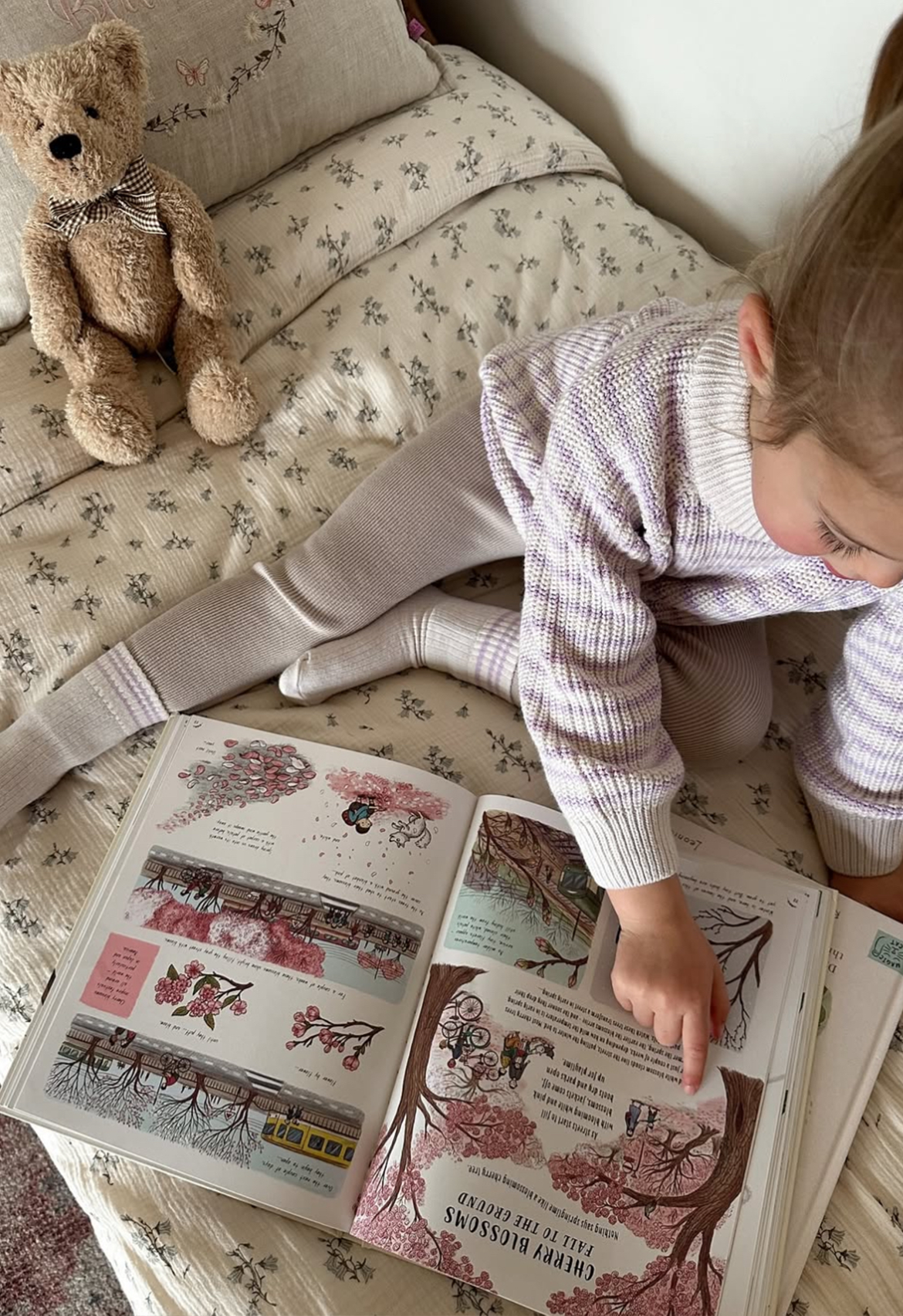 Child reading a book on a floral-patterned couch with a teddy bear beside them