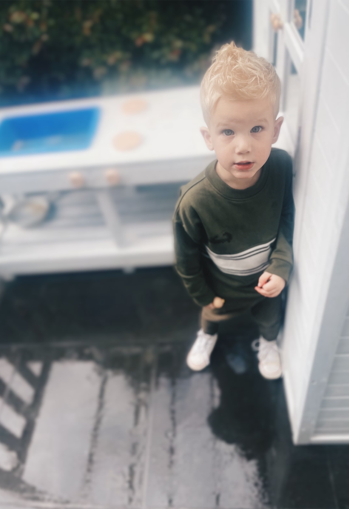 Young child standing on a wet pavement in olive tracksuit