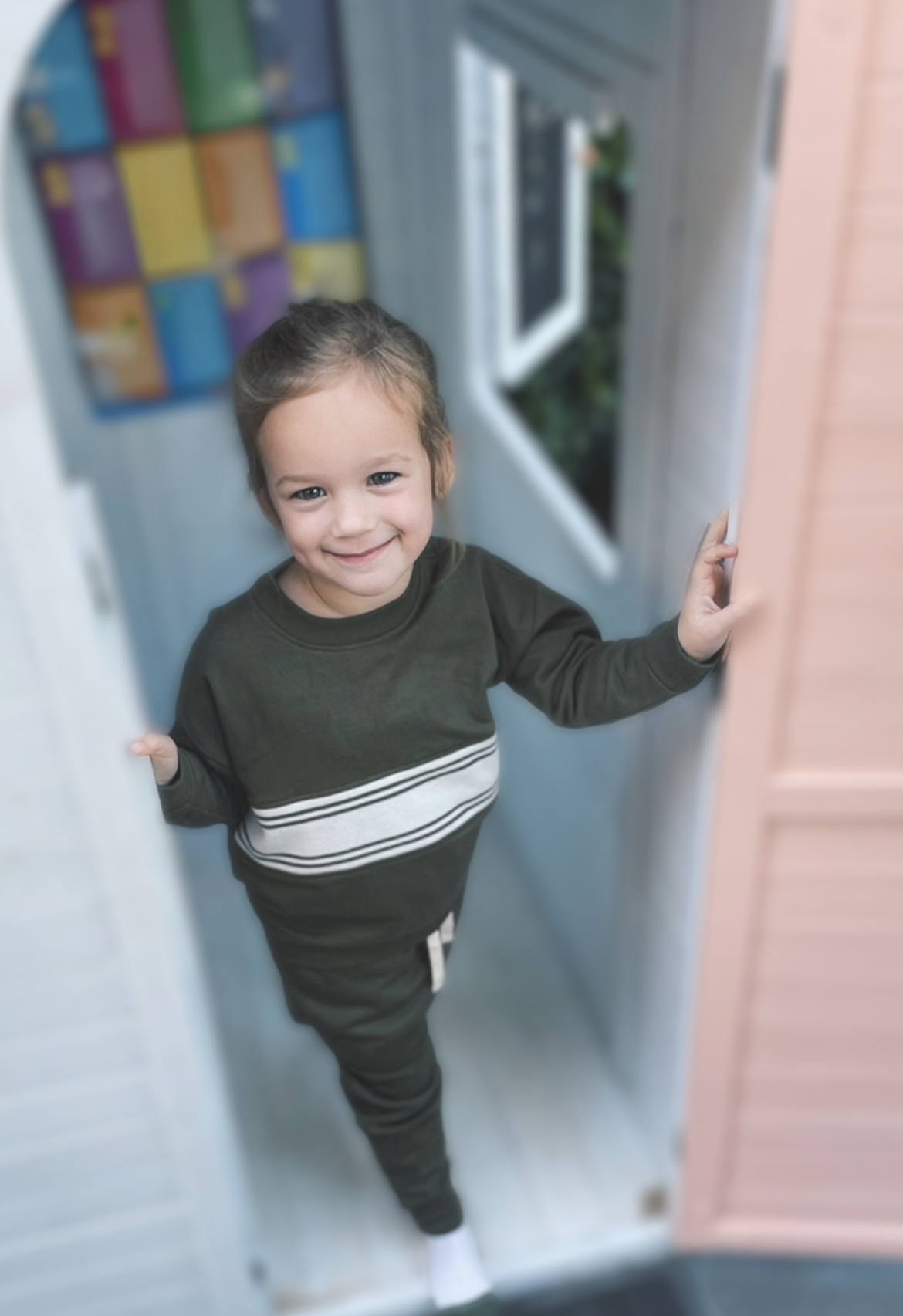 Child standing inside a cubby house wearing tracksuit
