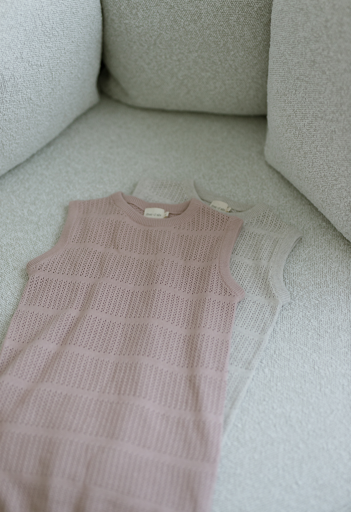 A cable knit dress in a faded rose color, displayed on a couch with a close-up texture shot.