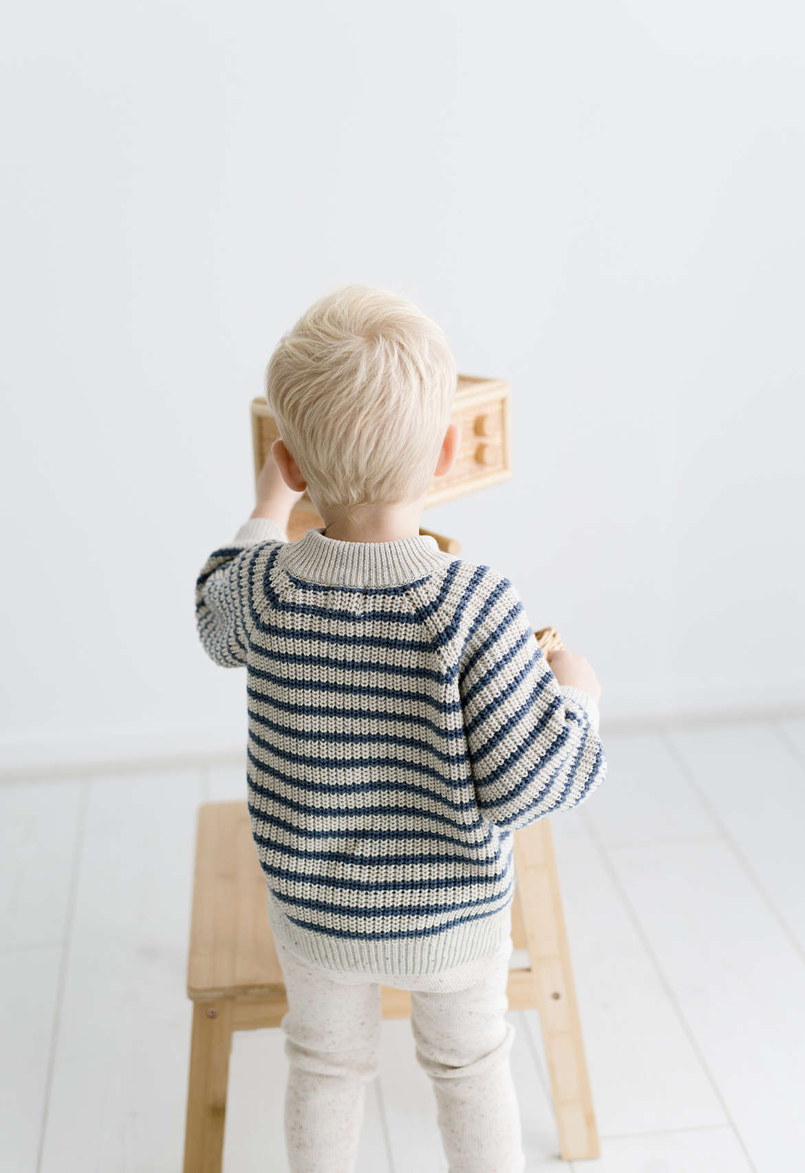 A child facing away from the camera is wearing a striped jumper with a speckle ivory base and deep ocean blue stripes.