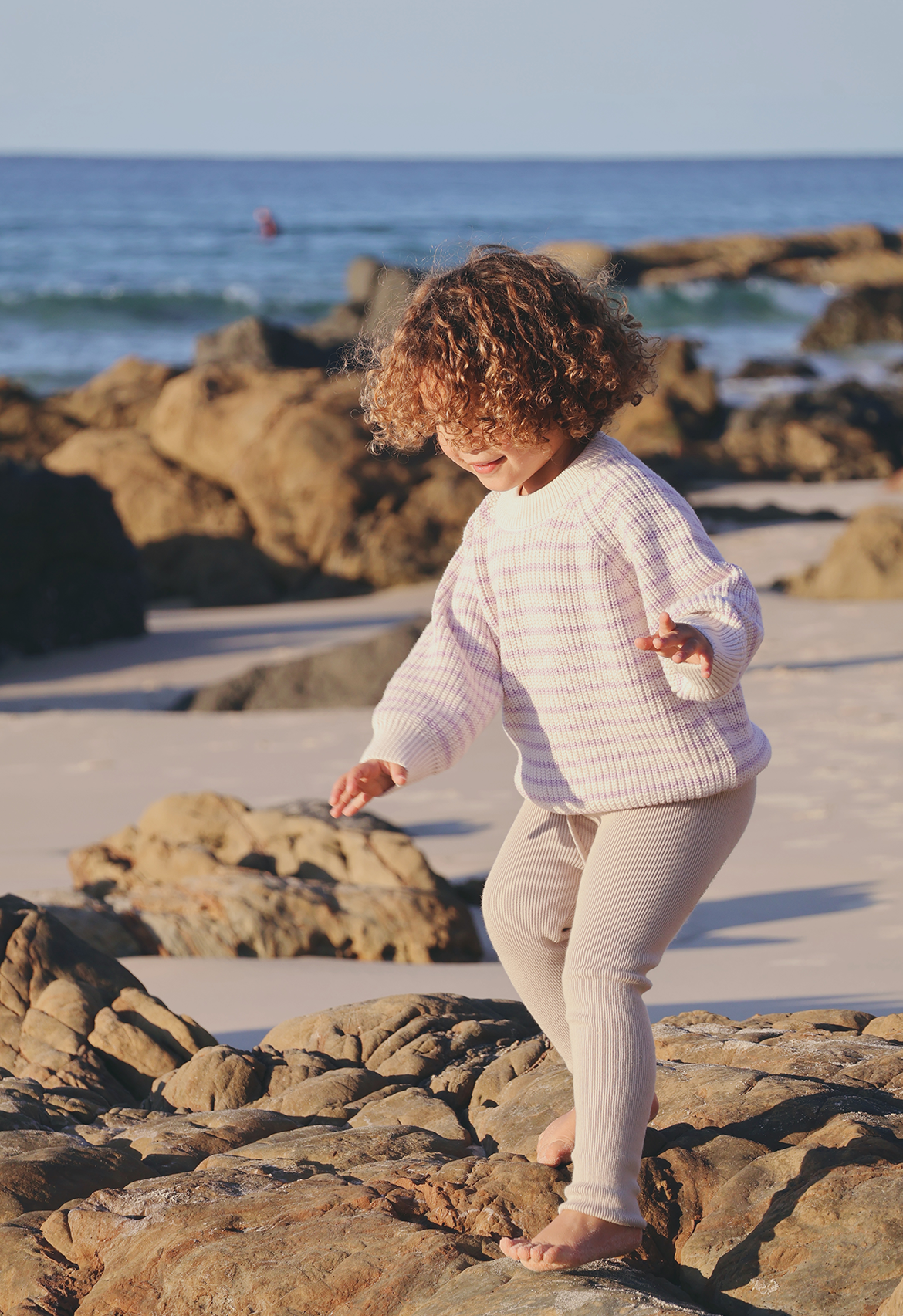 Child playing on rocks at the beach with ocean in the background