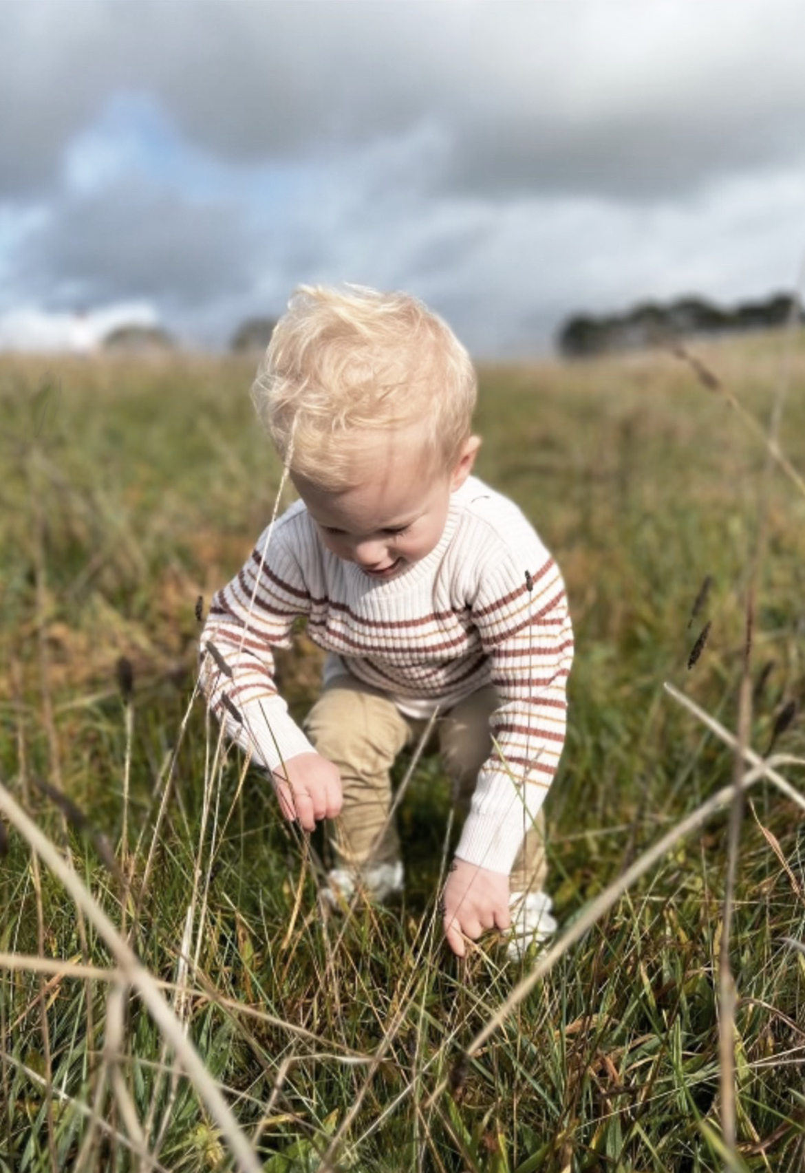 boy in field picking flowers in striped knit ribbed jumper