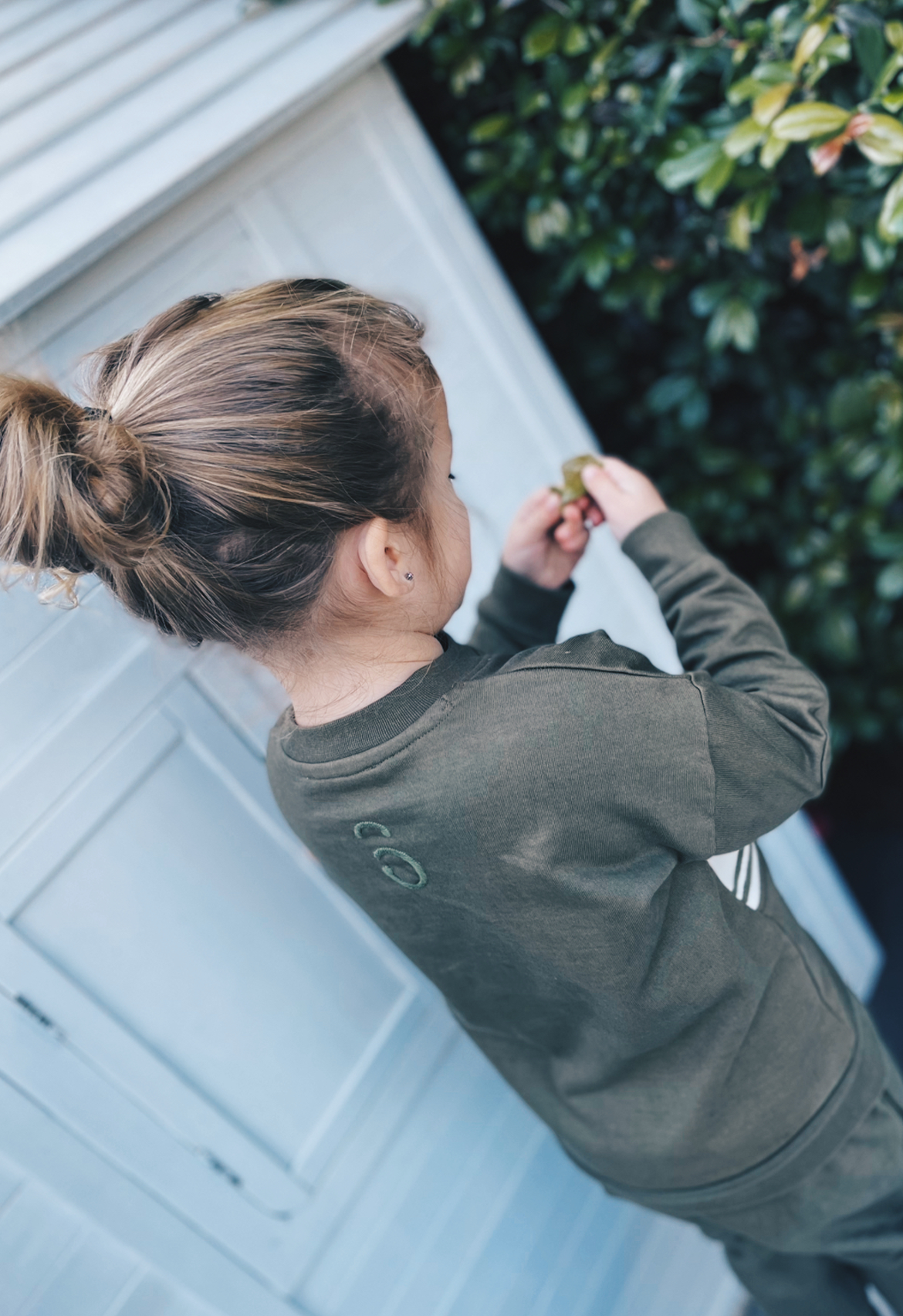 Child wearing an olive tracksuit standing outdoors.