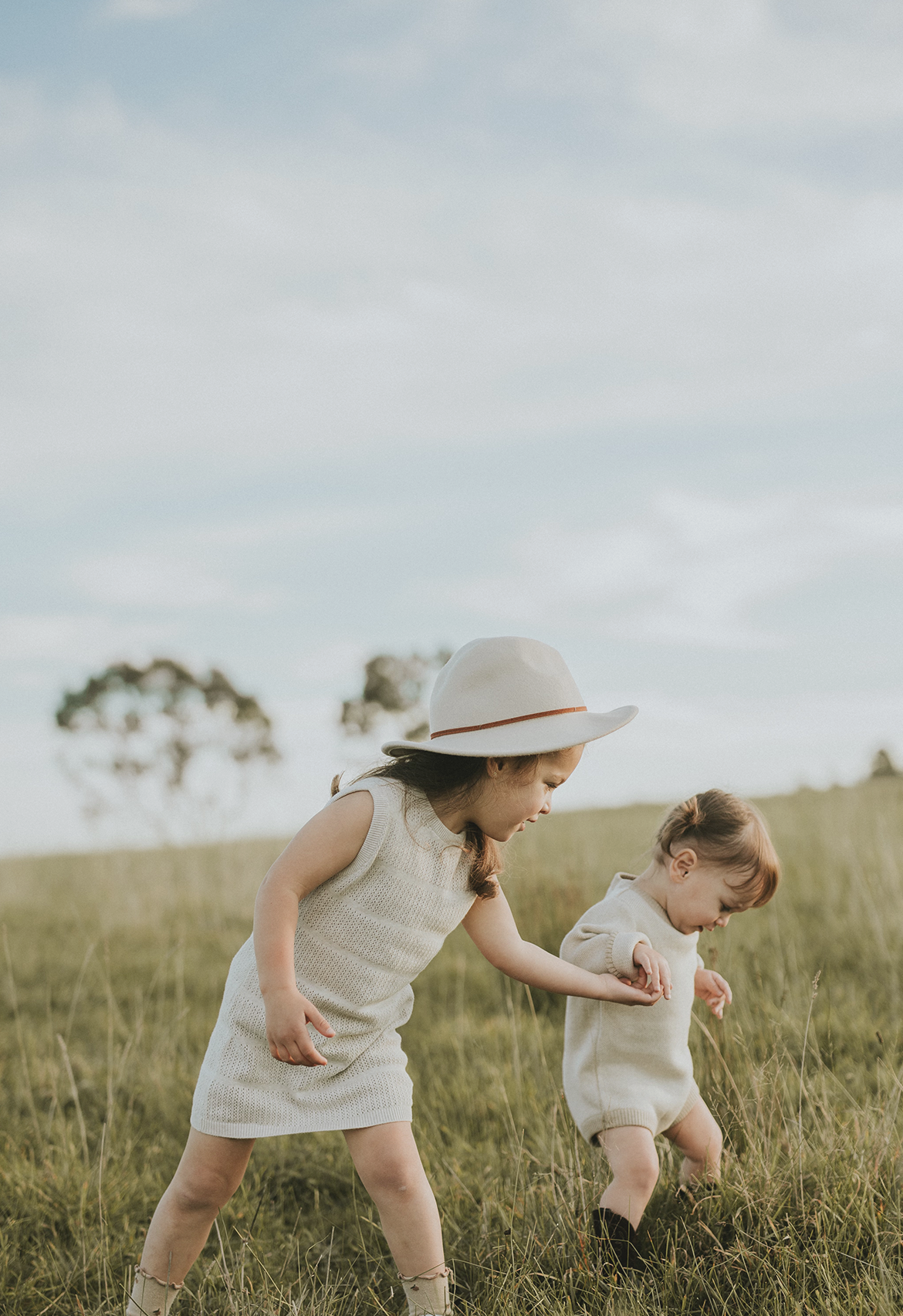 two toddler sisters holding hands in field paddock wearing dress