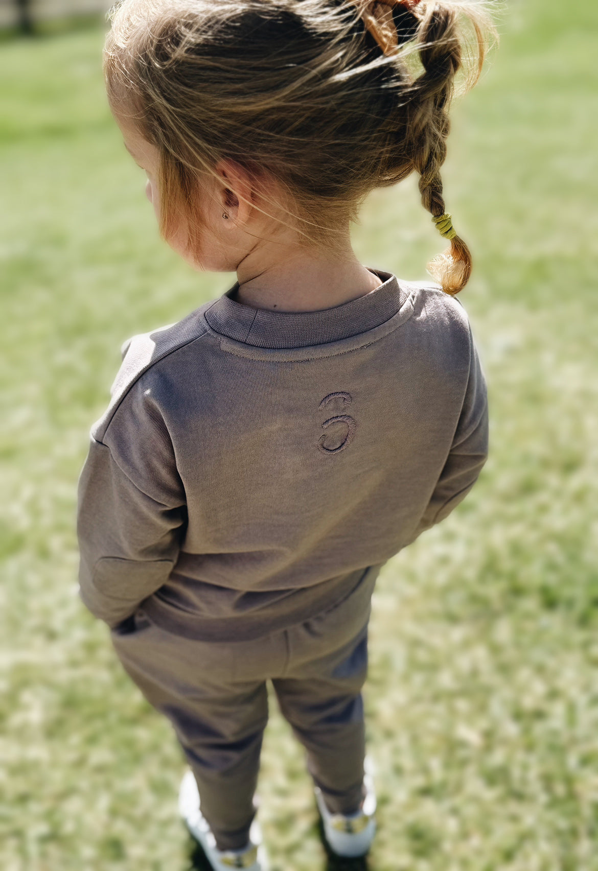 Child wearing a tracksuit with a logo, standing on grass