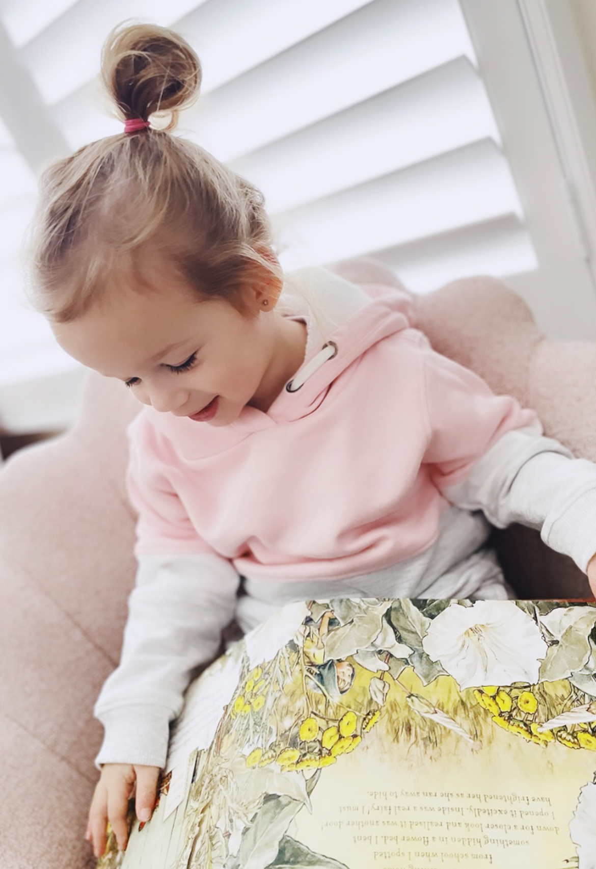 girl reading a book wearing a pink, grey and white block hooded jumper.