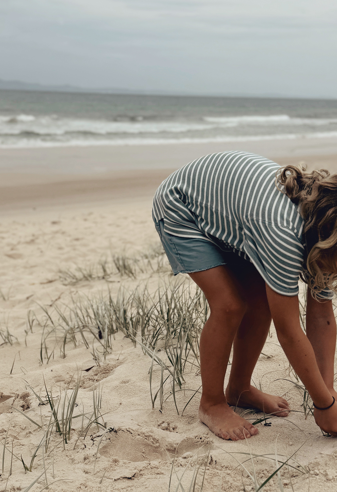 child on sand in teal and white stripe knit t-shirt