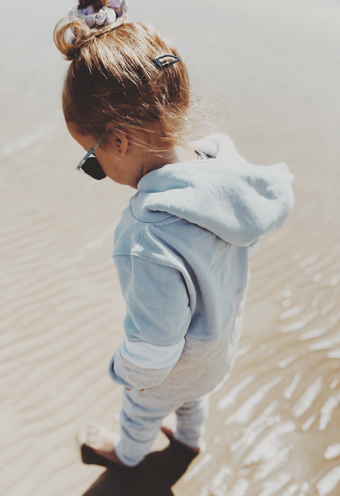 A child wearing a baby blue hoodie, standing by a water body.