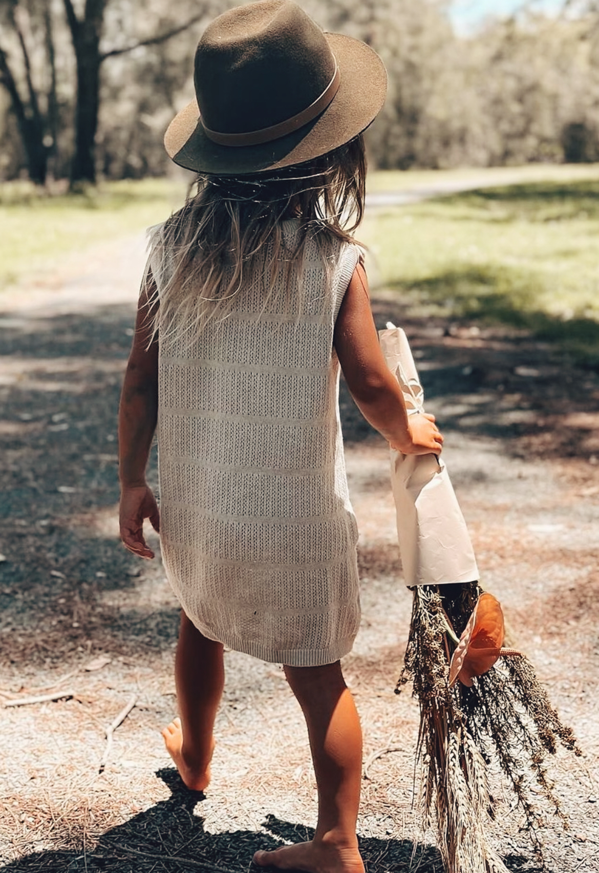 A child standing in a natural setting wearing a stone marle pointelle knit dress with a round neckline, sleeveless, and with a relaxed fit.
